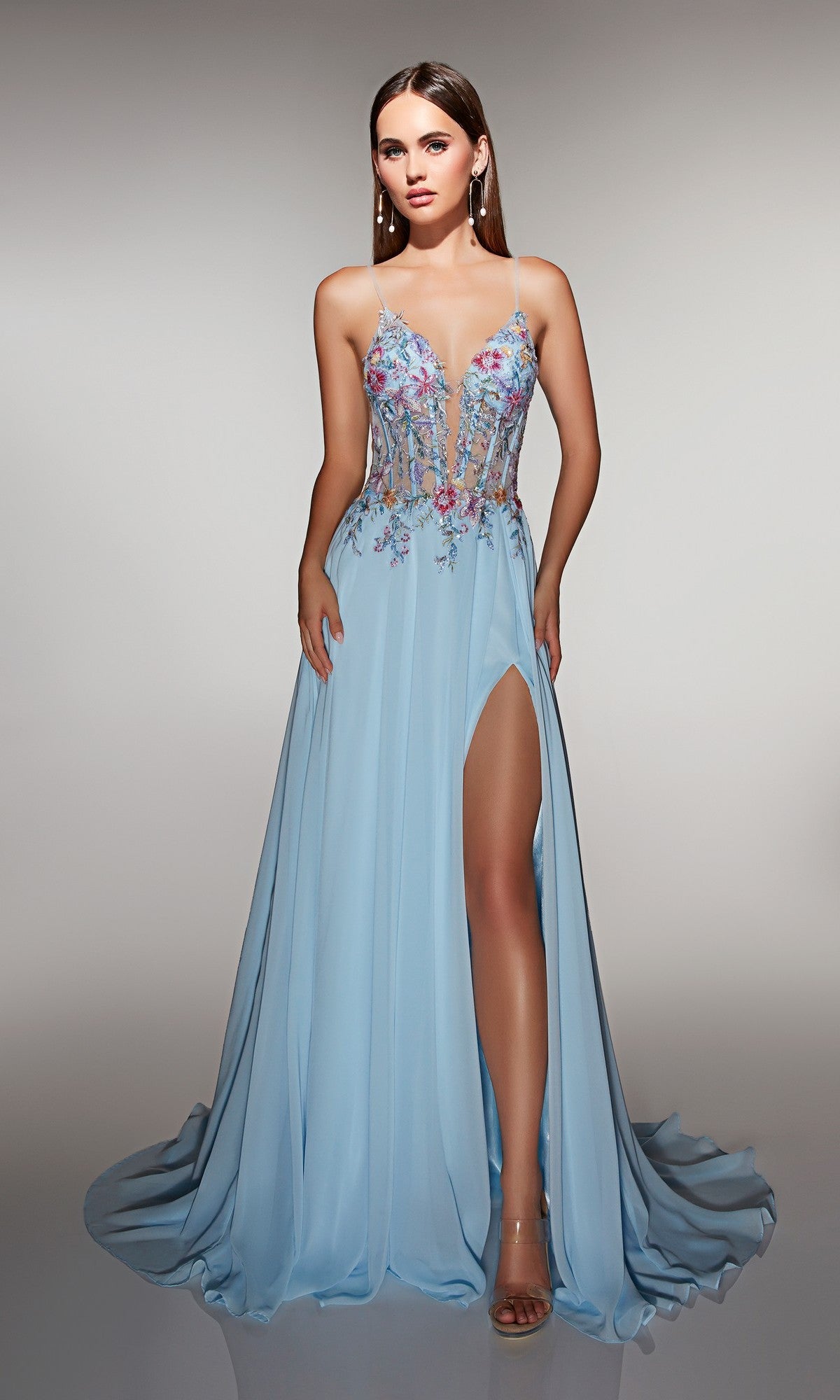 A woman wearing the Alyce 62179 Long Prom Dress in powder blue, featuring a sheer, floral-embroidered corset bodice, thin straps, and a high slit, stands against a neutral background.